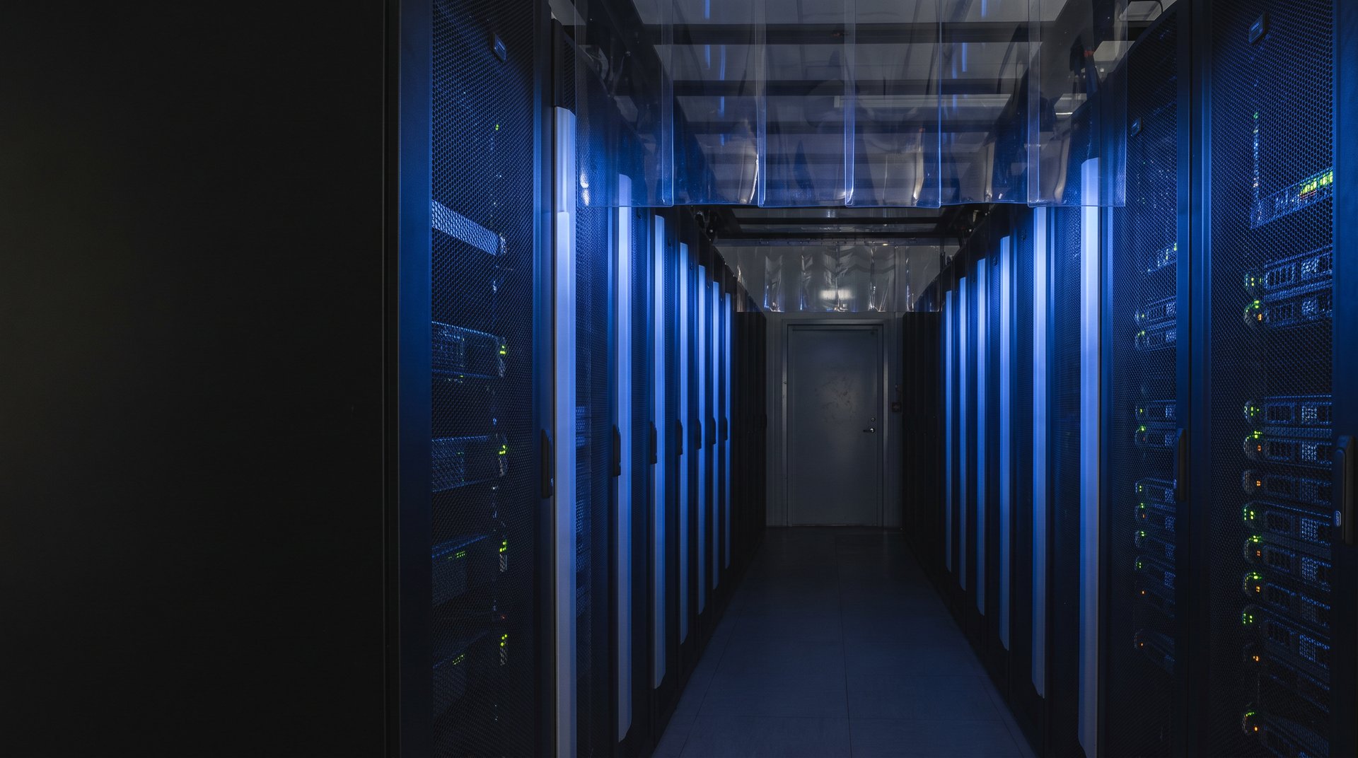 Datacenter aisle at night with two rows of server racks and cold-aisle containment overhead